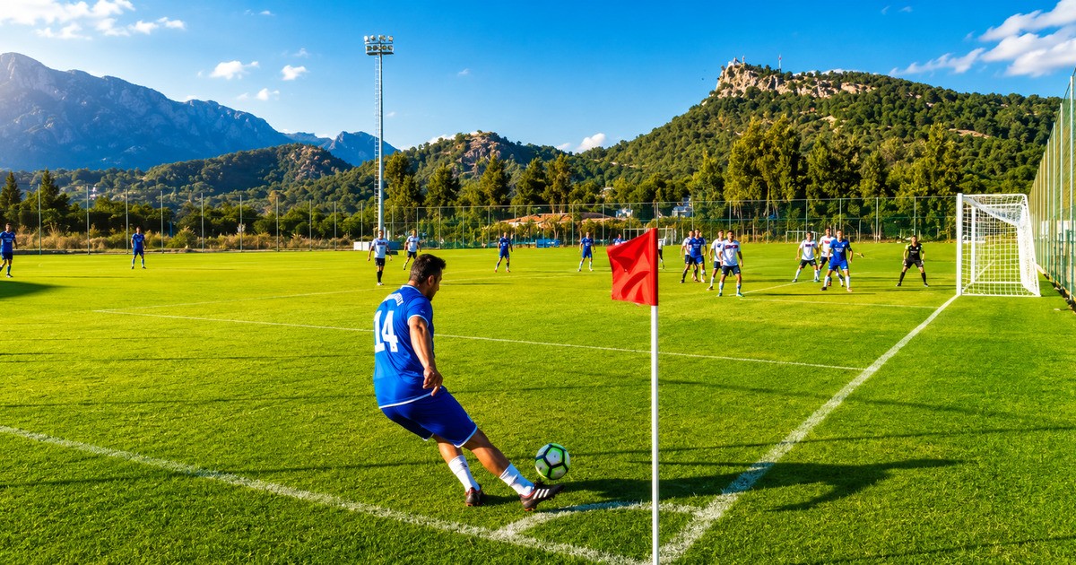 Football player taking a corner kick on a professional pitch in Kemer with mountain backdrop